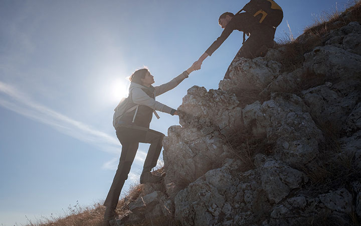man pulling a woman to help her climb a mountain. Cannabis SEO helps other digital marketing efforts.