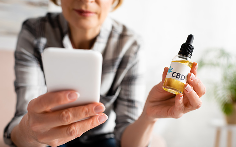 woman holding smartphone and bottle with cbd oil
